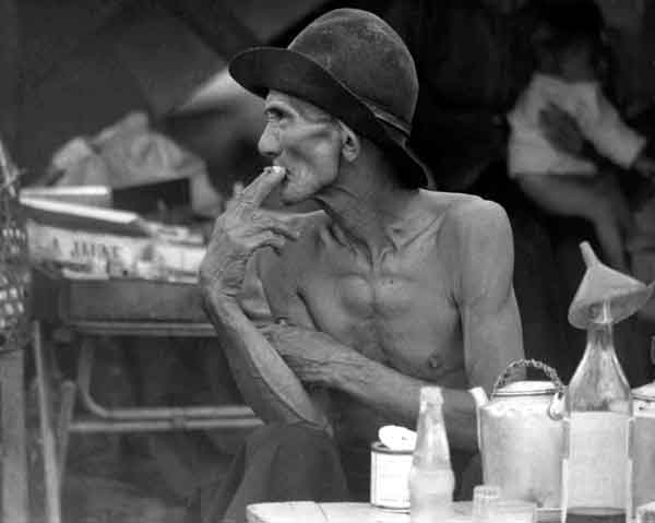 Skinny Shirtless Man Smoking at a Table