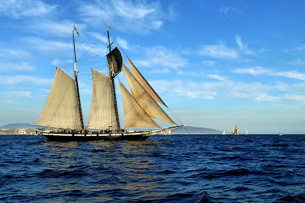 Three-masted ship with billowing sails against a blue sky