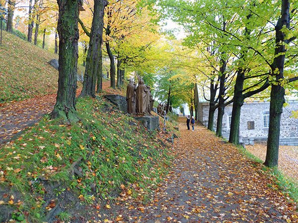 Two people photographing statues on a path with autumn foliage